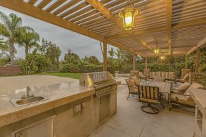 Outdoor kitchen and dining area under a pergola at the spacious patio of a home