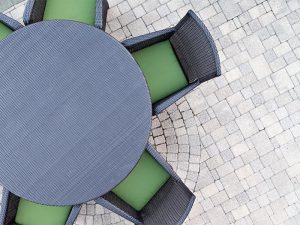 Six seater outdoor patio set with comfortable green cushions and a round dining table on a brick paved open-air patio with copyspace overhead view